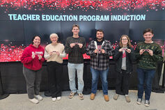 A group of students stands in front of a Teacher Education Program Induction sign.